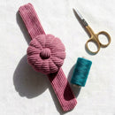 Dusty Rose Corduroy Pin Cushion with gold scissors and teal thread on a white background