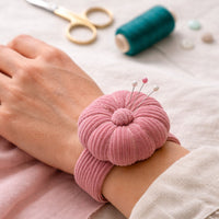 Dusty Rose Corduroy Pin Cushion on a wrist with sewing tools in the background