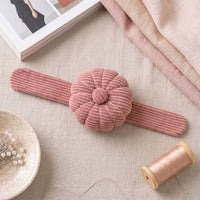 Dusty Rose Corduroy Pin Cushion on a textured surface with fabric and a spool of thread.