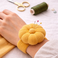 Sew Your Way Golden Butter corduroy pincushion on a wrist with sewing tools in the background