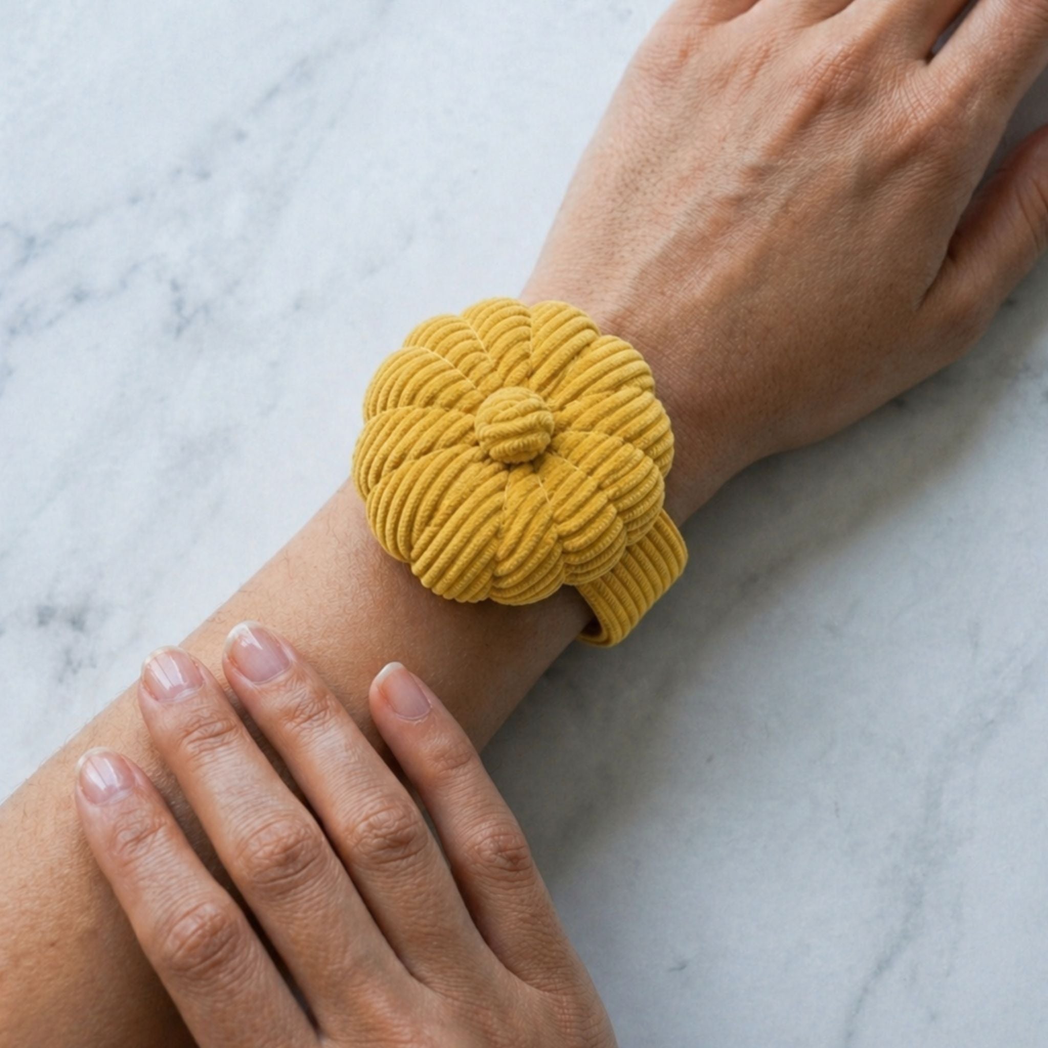 Yellow corduroy wristband on a person's wrist against a marble background
