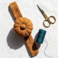 Honey Ochre corduroy pin cushion with gold scissors, and teal thread on a white background