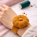 Honey Ochre corduroy pin cushion on a person's wrist with sewing tools in the background.
