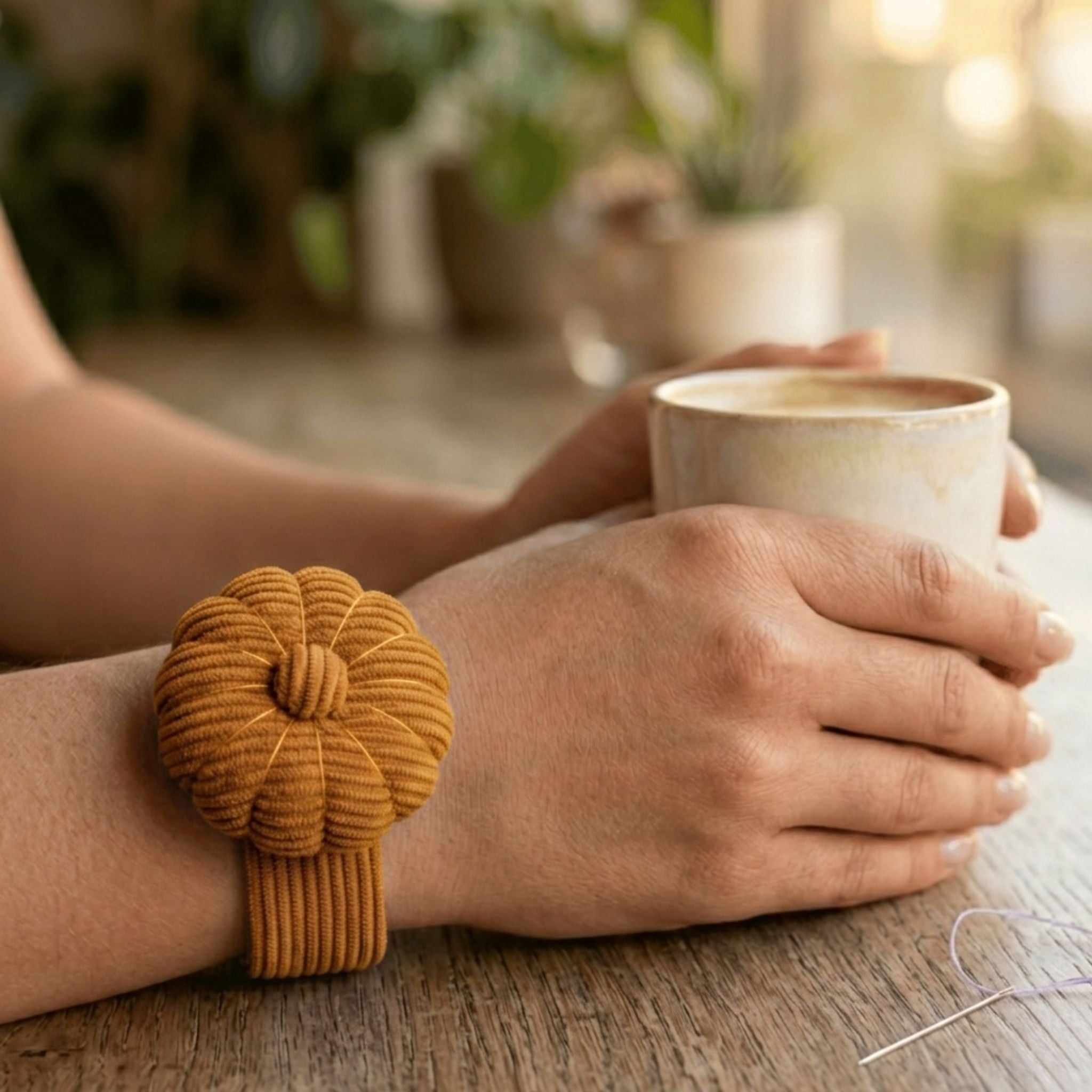 Person holding a mug with a Honey Ochre corduroy pin cushion on their wrist on a wooden surface