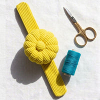 Yellow Limoncello colour corduroy pin cushion with scissors and spool of blue thread on a white background