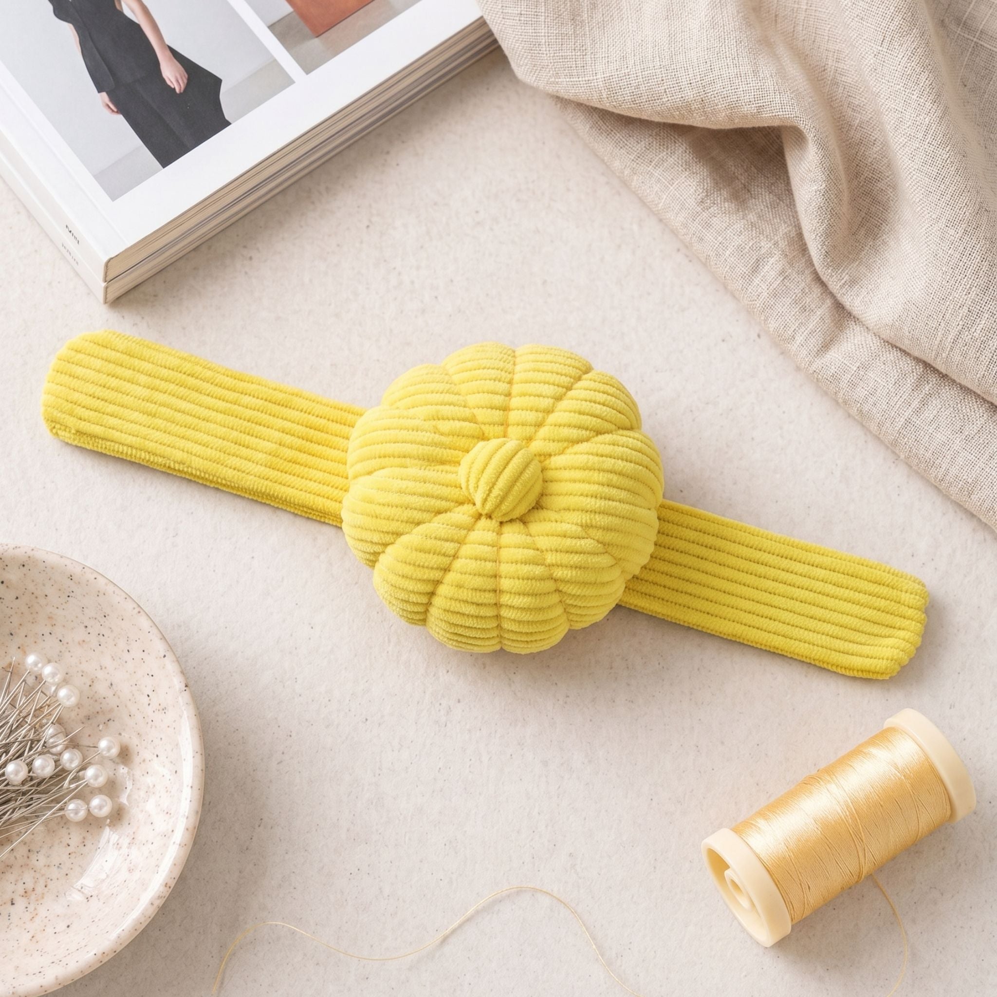 Yellow Limoncello colour corduroy pin cushion on a light surface with a spool of thread and a magazine in the background.