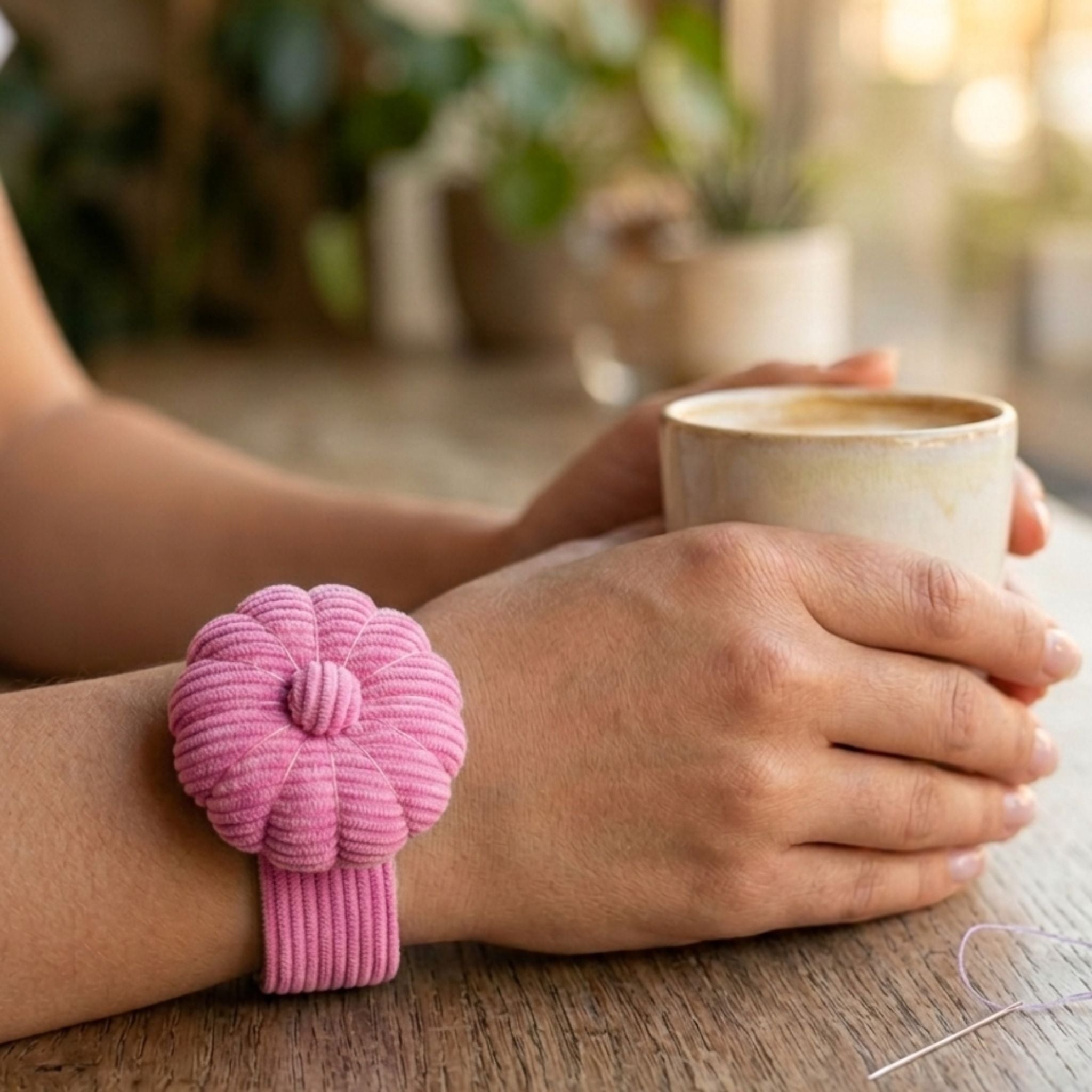 Person holding a mug with a Peony Pink Corduroy Pin Cushion on their wrist on a wooden surface