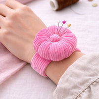 Pink pin cushion on a person's wrist with pins sticking out, on a light background.