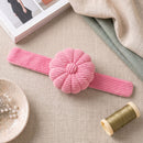 Peony Pink Corduroy Pin Cushion on a textured surface with a spool of thread and a book in the background.
