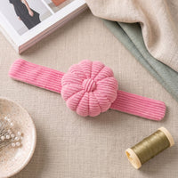 Peony Pink Corduroy Pin Cushion on a textured surface with a spool of thread and a book in the background.