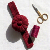 Rich Burgundy Corduroy Pin Cushion with gold scissors, and spool of thread on a white background
