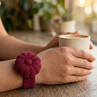 Person holding a mug with a Rich Burgundy Corduroy Pin Cushion wristband on a wooden surface