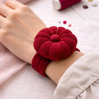 Rich Burgundy Corduroy Pin Cushion on a wrist with pins sticking out, on a light pink fabric background.