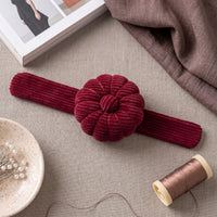Rich Burgundy Corduroy Pin Cushion on a textured surface with a spool of thread and fabric.