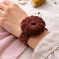 Brown pincushion on a wrist with pins, against a light background.