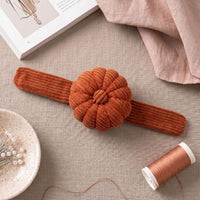 Terracotta Corduroy Pin Cushion on a beige fabric background