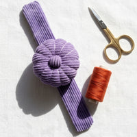 Wild Lilac Corduroy Pin Cushion with scissors and orange thread on a white background