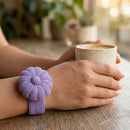 Person holding a cup wearing a Wild Lilac Pin Cushion on a wooden surface