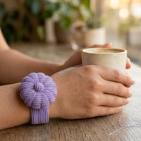 Person holding a cup wearing a Wild Lilac Pin Cushion on a wooden surface